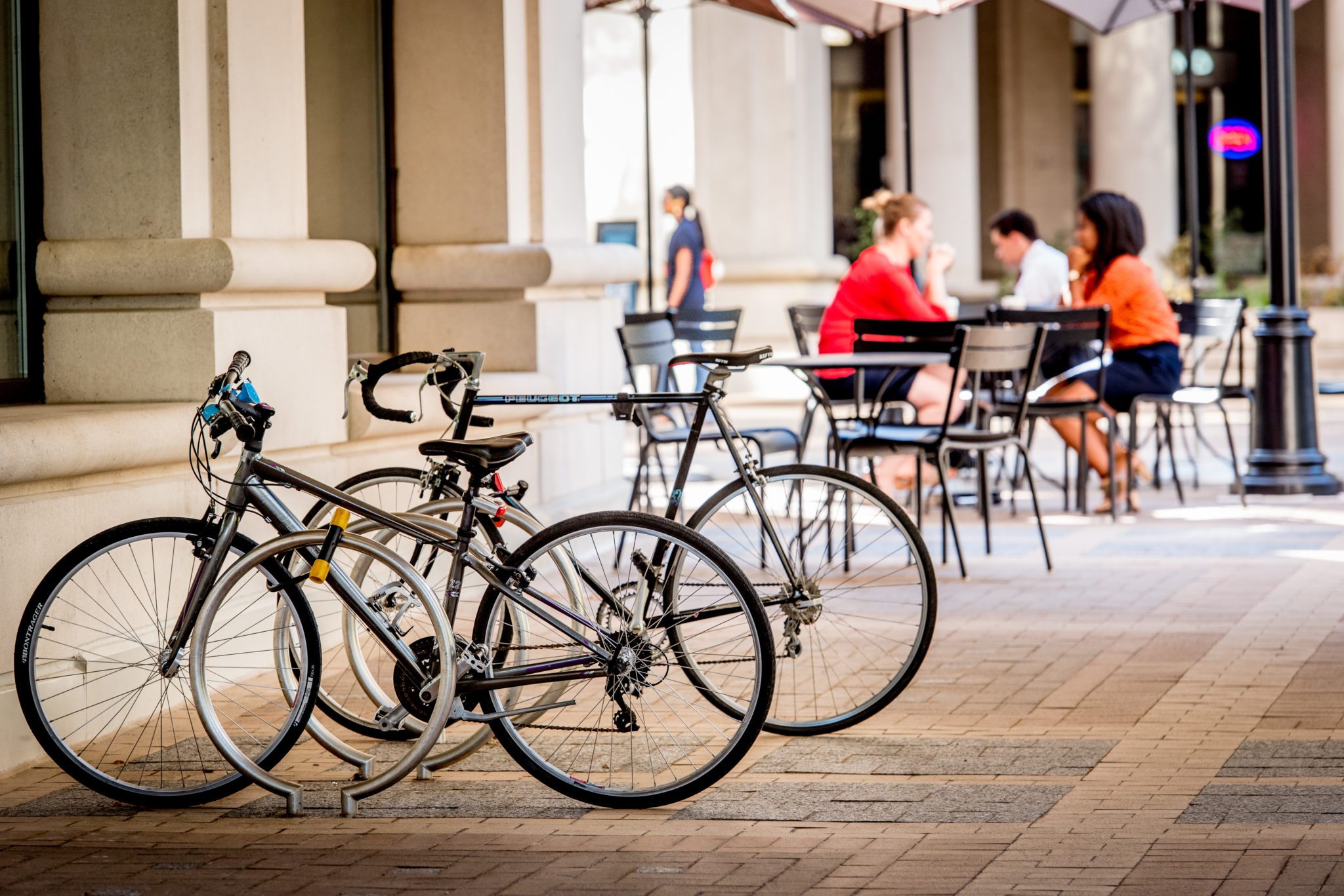 Two bike racks locked to racks in the foreground with people having coffee in the background