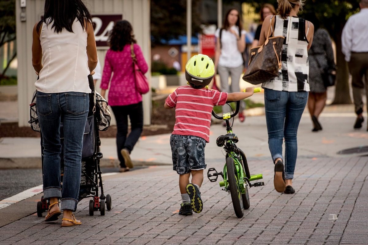 kid walking his bike on sidewalk with his mom