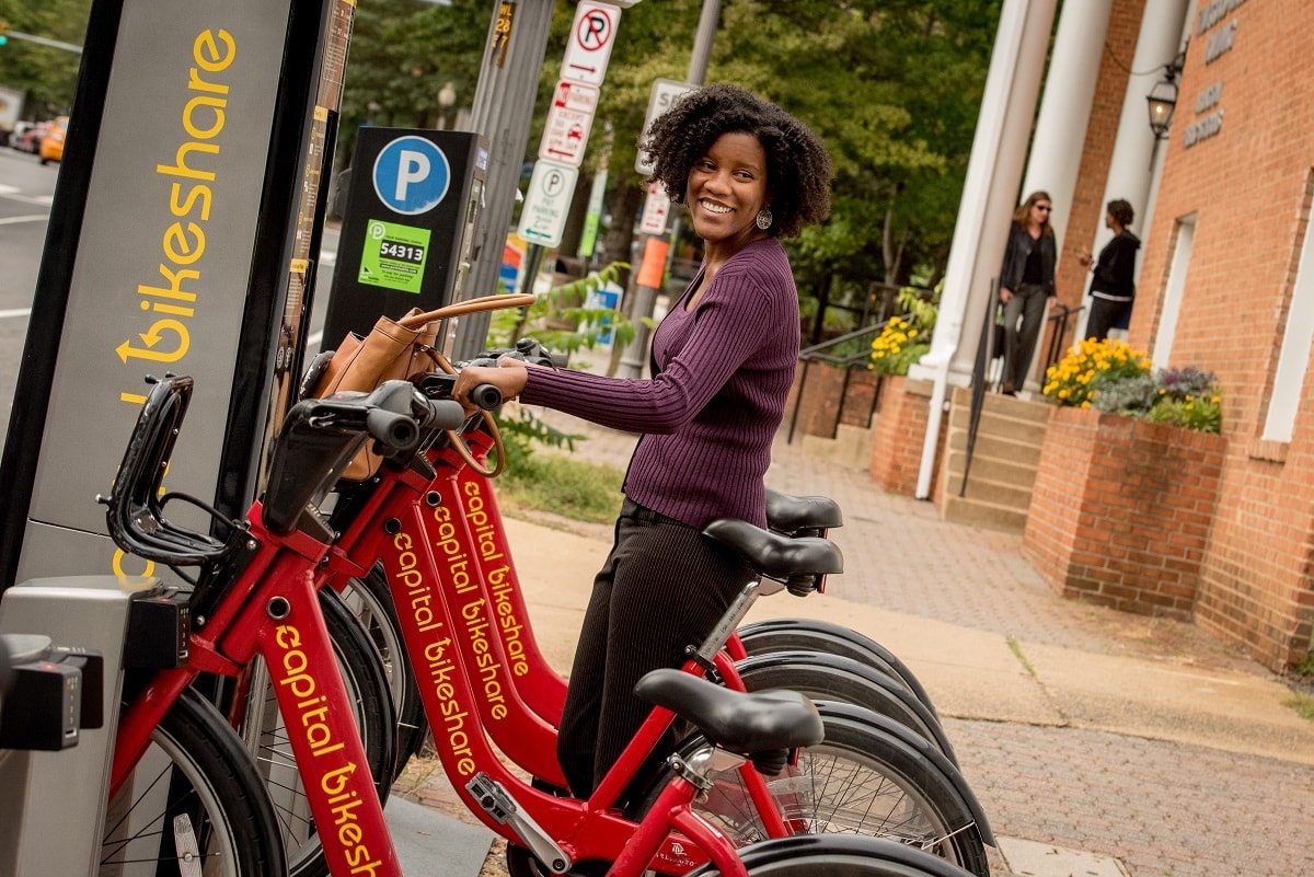 Woman smiling with hands on handle bar grips at a Bikeshare station, ready to check out a bike.