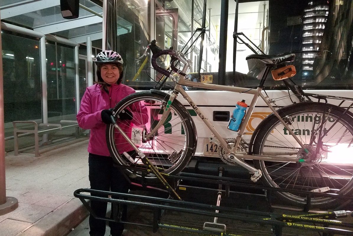 Susan poses with a bike on the bike rack of a bus.