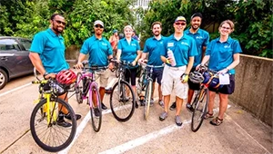 a group photo of cyclists hold their bikes in matching blue shirts