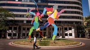 a photo of a large colorful public sculpture and a person walking by it on a sunny day