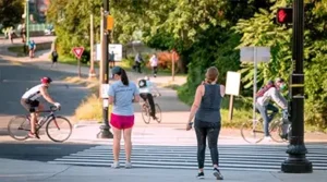 a photo of people and cyclists crossing the street on a sunny day
