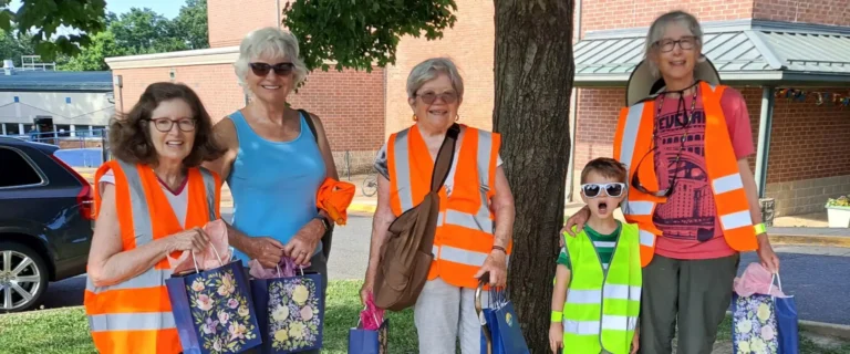 a photo of a group of women one of whom has their grandson with them. They have reflective vests on and are posing under a tree.