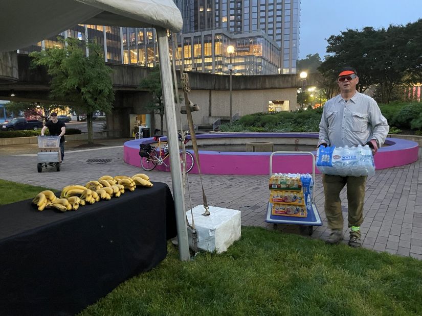 A person holding a case of bottled water setting up for an outdoor event.